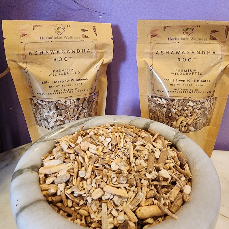 May include: Two brown paper bags filled with dried ashwagandha root. The bags have a white label with the text "Ashwagandha Root" and "Premium Wildcrafted". The text "85&deg;c | Steep 10-15 minutes" is also on the label. A white bowl filled with the dried root is in the foreground.