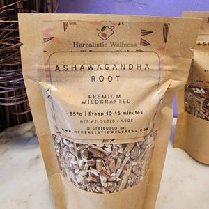 May include: A brown paper bag with a clear window showing dried ashwagandha root. The bag has a label that says "Herbalistic Wellness" and "Ashwagandha Root". The label also says "Premium Wildcrafted" and "85&deg;c | Steep 10-15 minutes". The net weight is 51.02g / 1.9oz. The bag is distributed by www.herbalisticwellness.com.