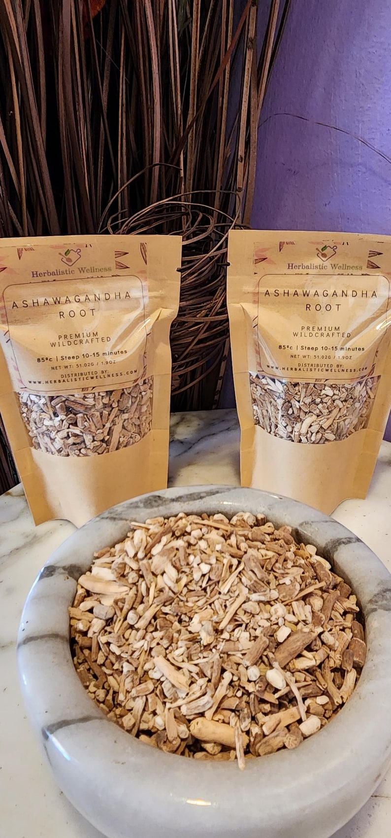 May include: Two brown paper bags filled with dried ashwagandha root. The bags have a white label with the text "Herbalistic Wellness Ashwagandha Root Premium Wildcrafted 85&deg;c | Steep 10-15 minutes Net Wt: 51.02g / 1.90z Distributed by Herbalistic Wellness.com". A white bowl filled with dried ashwagandha root is in the foreground.