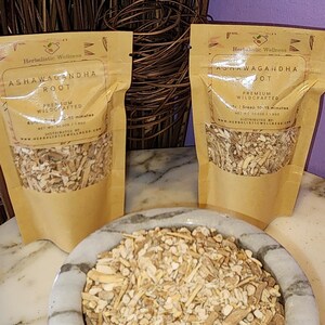 May include: Two brown paper pouches with white text that reads "Herbalistic Wellness Ashwagandha Root Premium Wildcrafted" and "Steep 10-15 minutes Net Wt 3.7 oz (105g)". A white ceramic bowl filled with light brown, dried root pieces.