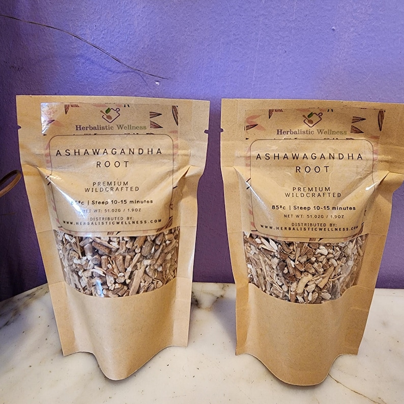 May include: Two brown paper pouches with clear windows showing dried herbs inside. The pouches are labeled "Ashwagandha Root" with the text "Premium Wildcrafted" and instructions for steeping the herbs. The text also includes "85&deg;c | Steep 10-15 minutes" and "Net Wt: 51.020 / 1.90Z".