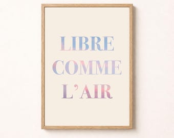 May include: A framed wall art print featuring the text LIBRE COMME L'AIR in a gradient of blue, purple, and pink colors. The lettering is set against a cream-colored background and enclosed within a simple, light-toned wooden frame.