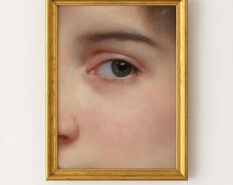 May include: A framed oil painting featuring a close-up view of a human eye and the bridge of a nose. The artwork is encased in a rectangular, metallic gold frame with a simple, classic molding, highlighting the detailed skin texture and iris.