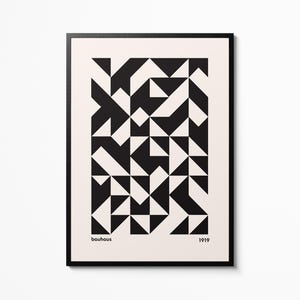 May include: Framed Bauhaus art print with a geometric design of black and white triangles and shapes. The word "bauhaus" and the year "1919" are printed at the bottom. The print is in a black frame, suitable for a modern interior.