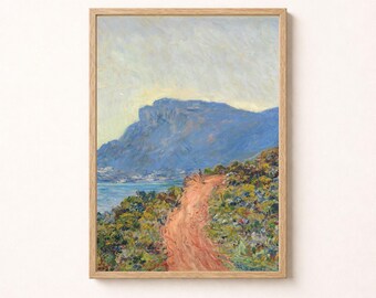May include: A framed landscape painting featuring a reddish-brown dirt path winding through green and yellow vegetation toward a large blue mountain. The scene includes a body of water near the base of the mountain under a pale, light-filled sky.