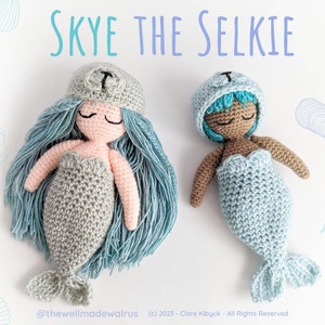 May include: Two crocheted mermaid dolls, one with light blue hair and a gray tail, the other with brown skin and a light blue tail. Both dolls are wearing crocheted hats with a letter "T" on them. The dolls are on a white background with a blue and white seashell pattern.