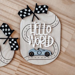 May include: Wooden sign featuring a race track design, a toy car, and the words "Hello World" in white lettering.