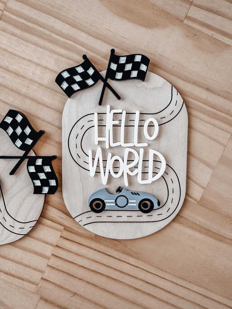May include: Wooden sign featuring a race track design, a toy car, and the words "Hello World" in white lettering.