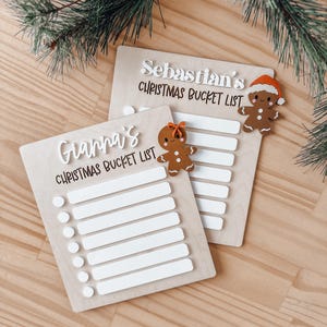 May include: Two wooden Christmas bucket list signs with gingerbread man ornaments. The signs are personalised with the names "Gianna's" and "Sebastian's".
