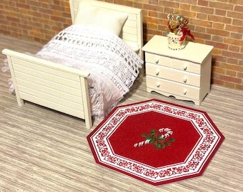 Könnte beinhalten: Miniatur-Schlafzimmer-Set mit weißem Bett, Nachttisch und einem rot-weißen Weihnachts-Teppich. Der Teppich zeigt ein Zuckerstangen- und Blumendesign. Das Bett hat eine weiße gehäkelte Decke und ein Kissen.