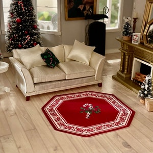 May include: A red and white octagonal rug with a candy cane and holly design in the center. The rug is on a light wood floor in a living room with a white couch, a small white table, and a Christmas tree.