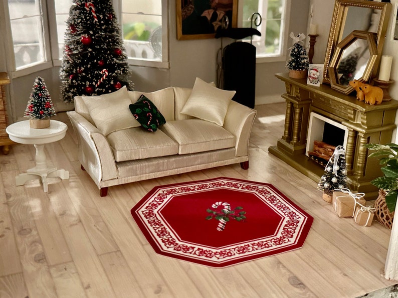 May include: A red and white octagonal rug with a candy cane and holly design in the center. The rug is on a light wood floor in a living room with a white couch, a small white table, and a Christmas tree.