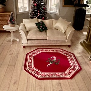 May include: A red and white octagonal rug with a candy cane design in the center. The rug is on a wooden floor in a living room with a white couch and a small Christmas tree.