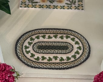 May include: A green and white oval rug with a shamrock pattern. The rug is made of braided rope and has a fringe border.