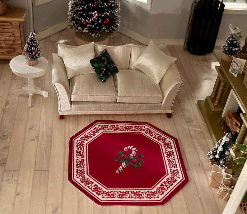 May include: A red and white octagonal rug with a candy cane design in the center. The rug is on a light wood floor in a room with a white couch and a small Christmas tree.
