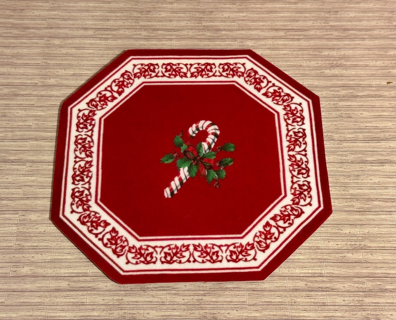 May include: Red octagonal rug with a white border and a candy cane design in the center. The candy cane is red and white with green holly leaves and red berries.