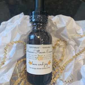 May include: A brown glass bottle with a black dropper top and a white label that reads "100% Natural - Handcrafted Arnica Flower Essence I let go my past & I accept to trust & re-connect with my physical & spiritual self love and joy Five drops three times a day"