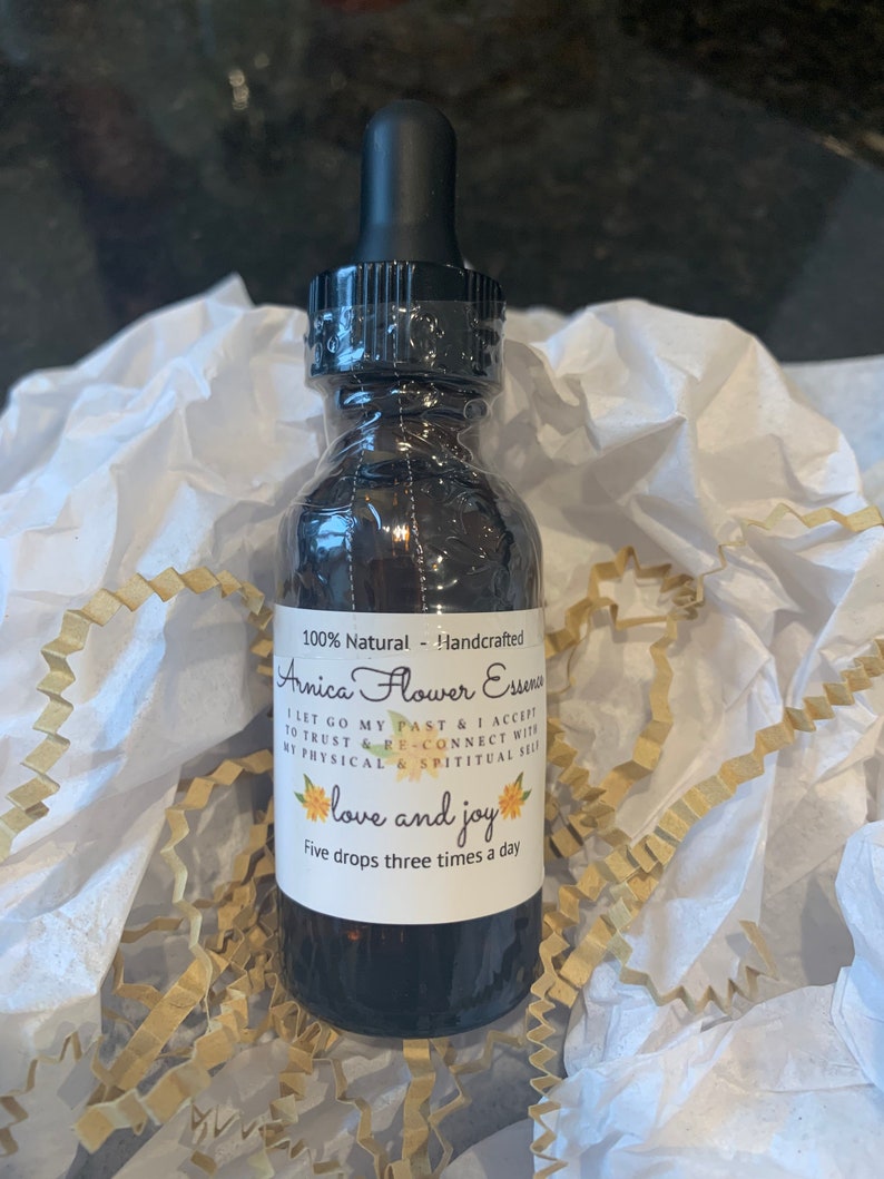 May include: A brown glass bottle with a black dropper top and a white label that reads "100% Natural - Handcrafted Arnica Flower Essence I let go my past & I accept to trust & re-connect with my physical & spiritual self love and joy Five drops three times a day"
