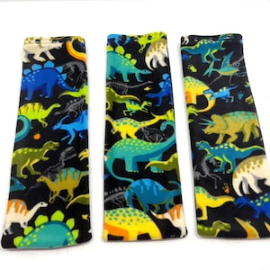 May include: Three rectangular fabric items with a black background and a colorful dinosaur pattern. The dinosaurs are in shades of blue, green, yellow, and white. The items are likely accessories or fabric pieces.