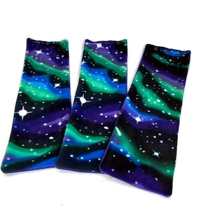 May include: Three long, rectangular fabric strips with a dark blue, green, and purple aurora borealis pattern. The fabric has a white speckled pattern of stars.