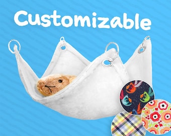 May include: A white, triangular pet hammock with silver metal rings, holding a small stuffed animal. The word "Customizable" is above the hammock. Three fabric swatches with colorful patterns are shown.