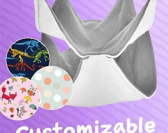 May include: A gray and white pet hammock with three fabric pattern options: dinosaur skeletons on navy, polka dots, and woodland creatures. The word "Customizable" is written in white script at the bottom.