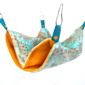 May include: A teal and orange patterned hammock for small pets, with two clips on each side for hanging.