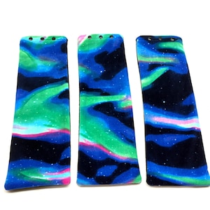 May include: Three rectangular fabric pieces with a vibrant aurora borealis design. The pattern features swirling blues, greens, and pinks against a dark background, with small holes at the top.