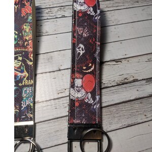 May include: Two black and red keychains with a silver key ring. The keychains feature a variety of horror movie characters, including Pennywise the clown, Freddy Krueger, and Jason Voorhees.