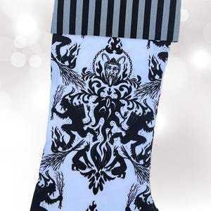 May include: A white Christmas stocking with a black and white pattern of a devil's head and two demons holding torches. The stocking has a black and white striped cuff.