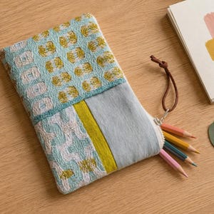 Peut inclure: Une trousse rectangulaire zippée avec un motif tissé texturé bleu sarcelle et blanc sur la moitié supérieure, une bande verticale vert citron et un panneau bleu clair uni sur le bas. Une tirette en cuir marron est fixée à la fermeture éclair.