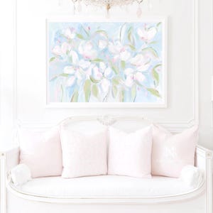 May include: A rectangular wall art print featuring an impressionistic floral painting with white blossoms, soft green leaves, and light blue brushstrokes, encased in a simple white frame and displayed above a white settee with four light pink pillows.
