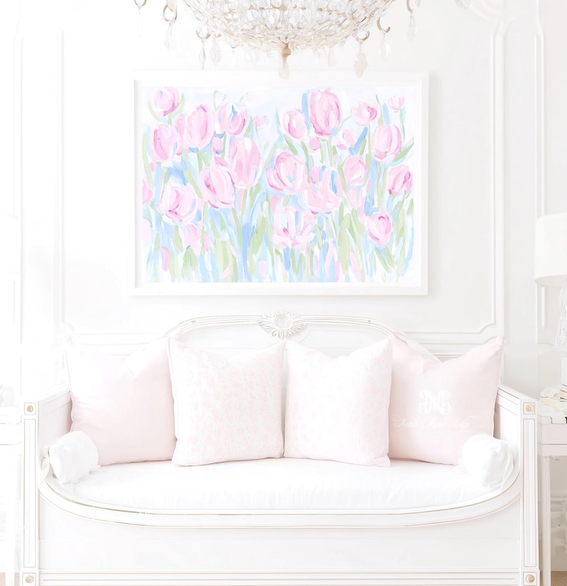 May include: A rectangular wall art print featuring an abstract painting of pink tulips with green and blue stems and leaves. The artwork is displayed in a white frame and hangs above a white settee adorned with four light pink throw pillows.