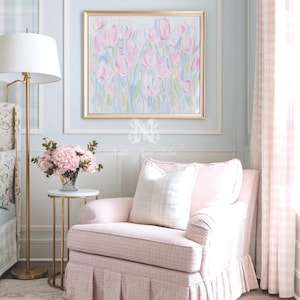 May include: A framed painting of pink tulips in a gold frame hangs above a light pink upholstered armchair with a pleated skirt. The chair features a white plaid throw pillow. A gold floor lamp and a small table with pink flowers are nearby.