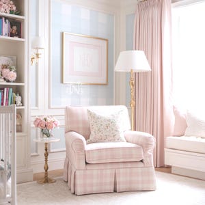 May include: A light pink and white plaid upholstered armchair with a pleated skirt and a floral patterned throw pillow. The chair is positioned in a room with light blue and white checkered wallpaper, a gold floor lamp, and a small side table.