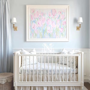 May include: A white wooden crib with vertical slats, a ruffled beige bed skirt, and a mattress featuring a grey and white floral pattern. Two matching floral pillows sit inside the crib, positioned beneath a framed painting of pink tulips.