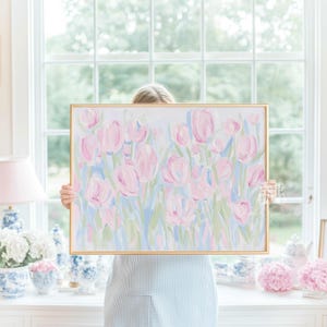 May include: A white crib with a light blue trim and a matching crib skirt. The crib is decorated with pink bows and floral pillows. Above the crib is a framed painting of pink tulips.