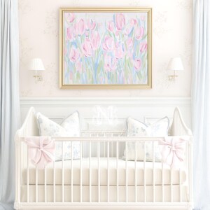 May include: A white wooden crib featuring a solid cream-colored mattress and skirt, adorned with two large pale pink bows on the front corners. Two square pillows with a blue floral pattern rest inside against the back of the crib frame.