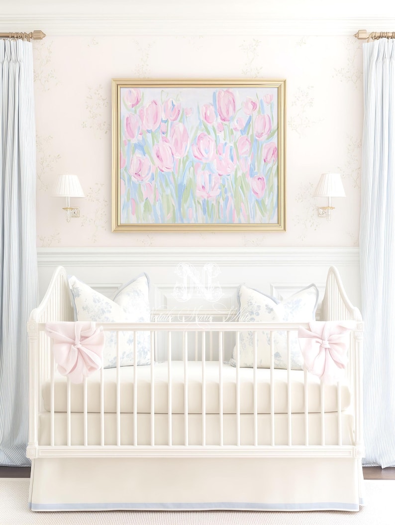May include: A white wooden crib featuring a solid cream-colored mattress and skirt, adorned with two large pale pink bows on the front corners. Two square pillows with a blue floral pattern rest inside against the back of the crib frame.