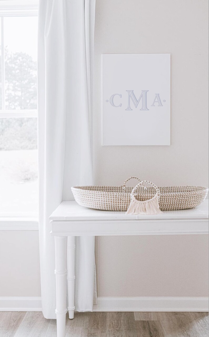 May include: A white wicker bassinet with a white and beige woven design, a white table with a white top and bamboo legs, and a white canvas with the text "CMA" in gray lettering.