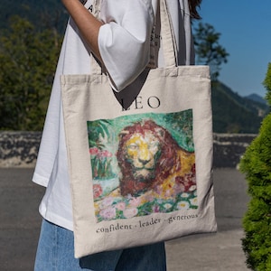 Peut inclure: Un sac fourre-tout en toile blanche avec une illustration de lion colorée et le texte "LEO confident - leader - generous".