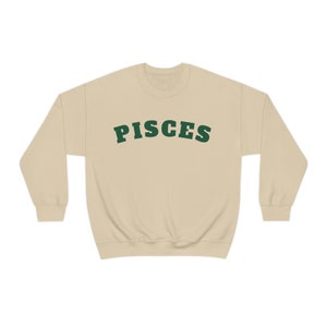 May include: A beige sweatshirt with the word "PISCES" printed in green on the front.