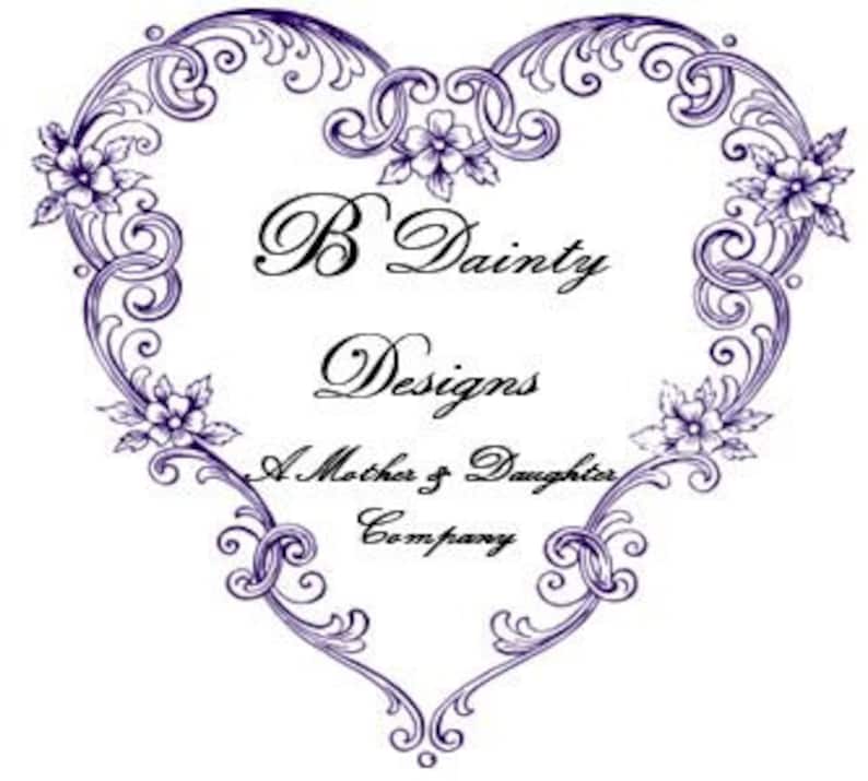 Puede incluir: Un dise&ntilde;o morado en forma de coraz&oacute;n con detalles florales y el texto "B Dainty Designs, A Mother & Daughter Company". El dise&ntilde;o presenta remolinos ornamentados e ilustraciones de flores delicadas, perfecto para un logotipo o emblema.