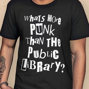 May include: Black t-shirt with white text that reads "Whats More Punk Than The Public Library?". The shirt is a crew neck style and is being worn by a person. The Midnight Laundry logo is on the left side.