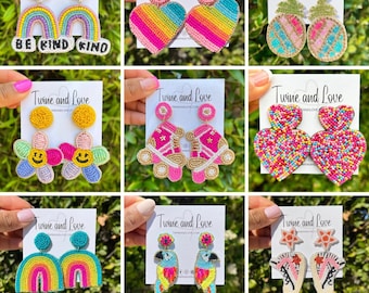 Op de afbeelding: Negen paar kleurrijke kralen oorbellen. De oorbellen worden getoond op kaarten met de tekst "Twine and Love" en het websiteadres "twineandlove.com". De oorbellen hebben verschillende ontwerpen, waaronder regenbogen, harten, bloemen, rol schaatsen en papegaaien.