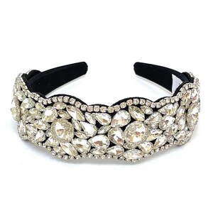 May include: A black headband with a wide band of clear rhinestones. The rhinestones are arranged in a wavy pattern and are of various sizes.