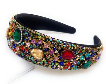 May include: A black headband with a wide band adorned with colorful rhinestones and large, faceted gems. The gems are in shades of green, red, blue, pink, and gold.