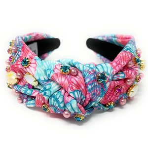 May include: A pink and blue floral headband with a knotted design and embellished with pearls and rhinestones.