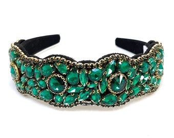 May include: A black headband with a wide band of emerald green rhinestones. The rhinestones are set in gold metal.