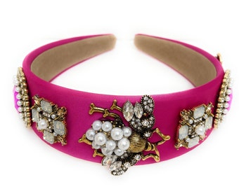May include: A pink satin headband with a gold bee and pearl embellishments.
